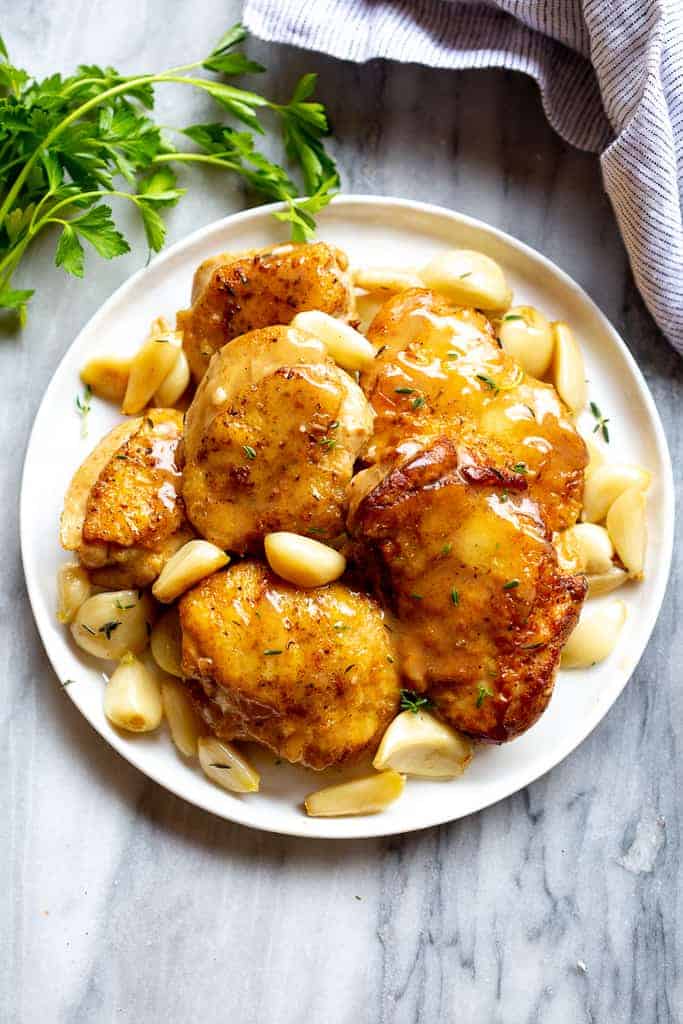 A plate filled with golden browned chicken thighs, garlic cloves and a creamy sauce.