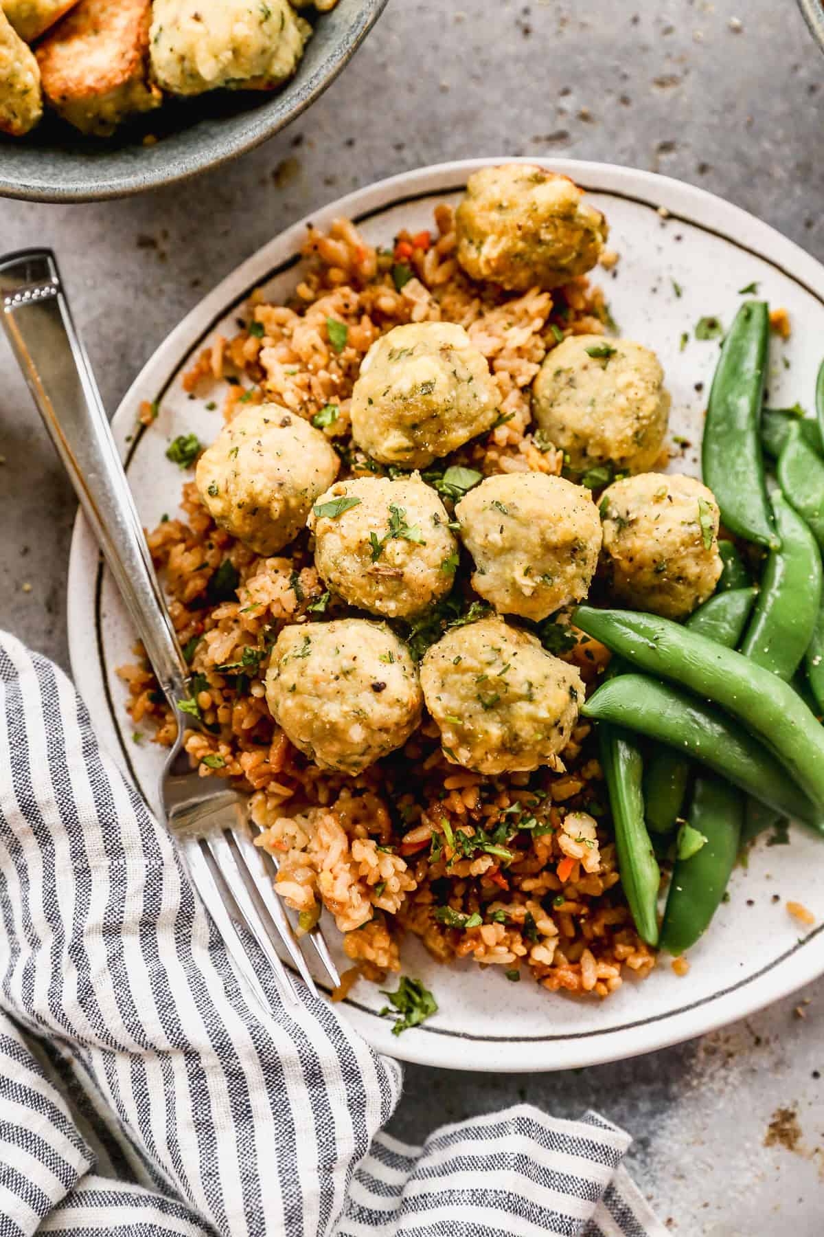 Homemade Baked Chicken Meatballs served on a plate on top of wild rice pilaf and cooked green beans.
