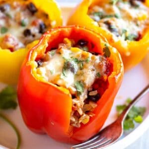 Three vegetarian stuffed peppers on a plate with a bite taken out of one to show the inside.