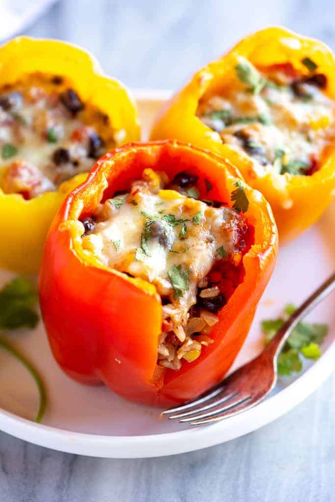 Three vegetarian stuffed peppers on a plate with a bite taken out of one, showing the filling inside.