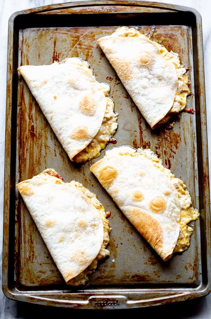 A sheet pan with for folded tortillas with chicken and cheese inside.