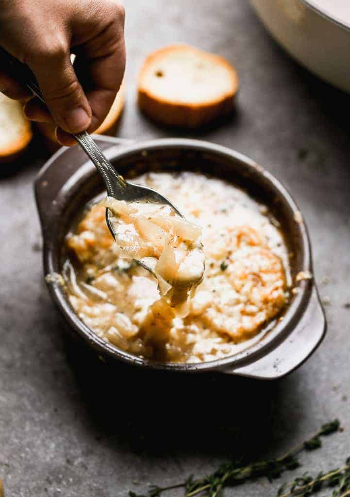 A hand spooning french onion soup from a bowl.
