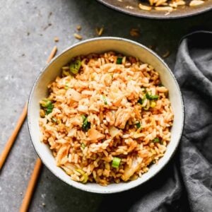 A bowl of kimchi fried rice with a skillet and chopsticks next to it.
