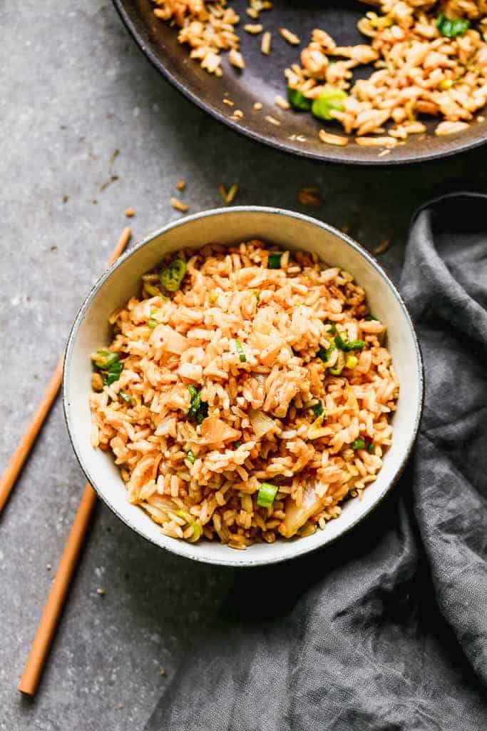 A bowl of kimchi fried rice with a skillet and chopsticks next to it.