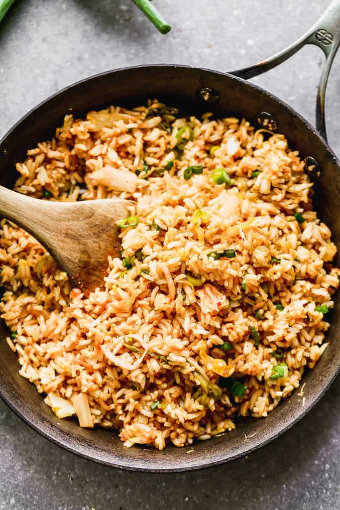 A skillet filled with kimchi fried rice and a wooden spoon in it for serving.