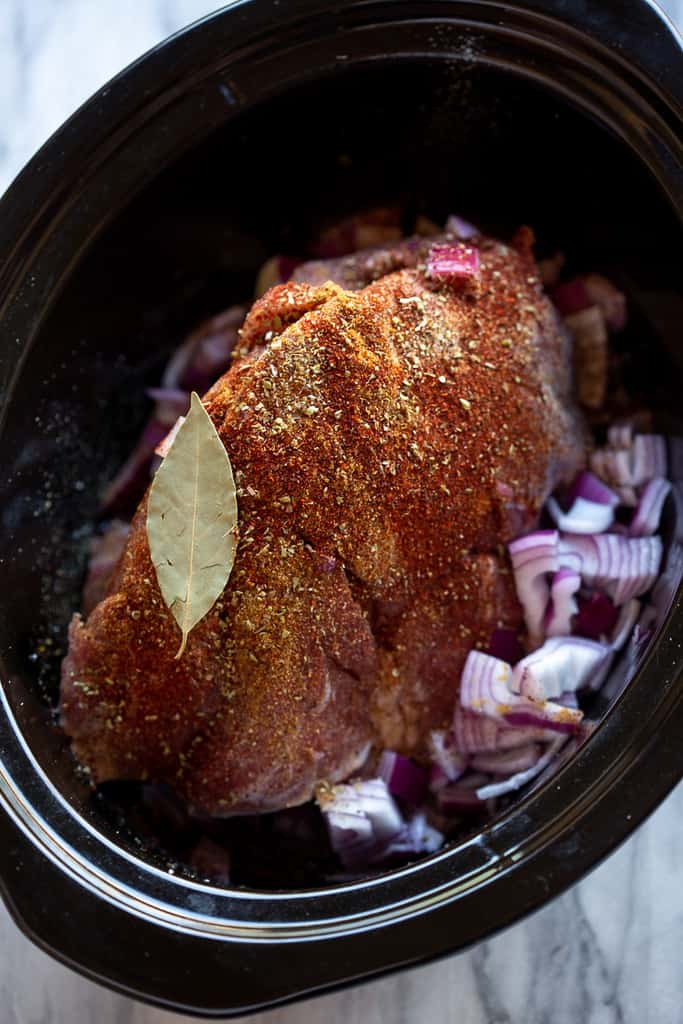 Pork roast in a slow cooker with spices, onion and a bay leaf.