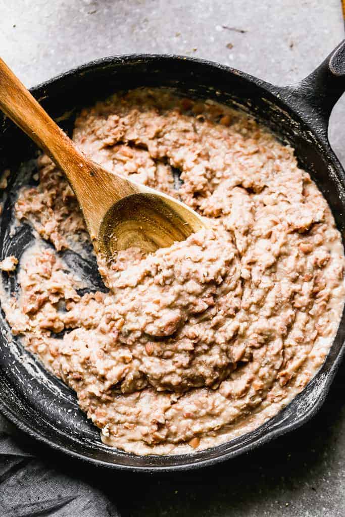 A skillet of refried beans with a wooden spoon in it.