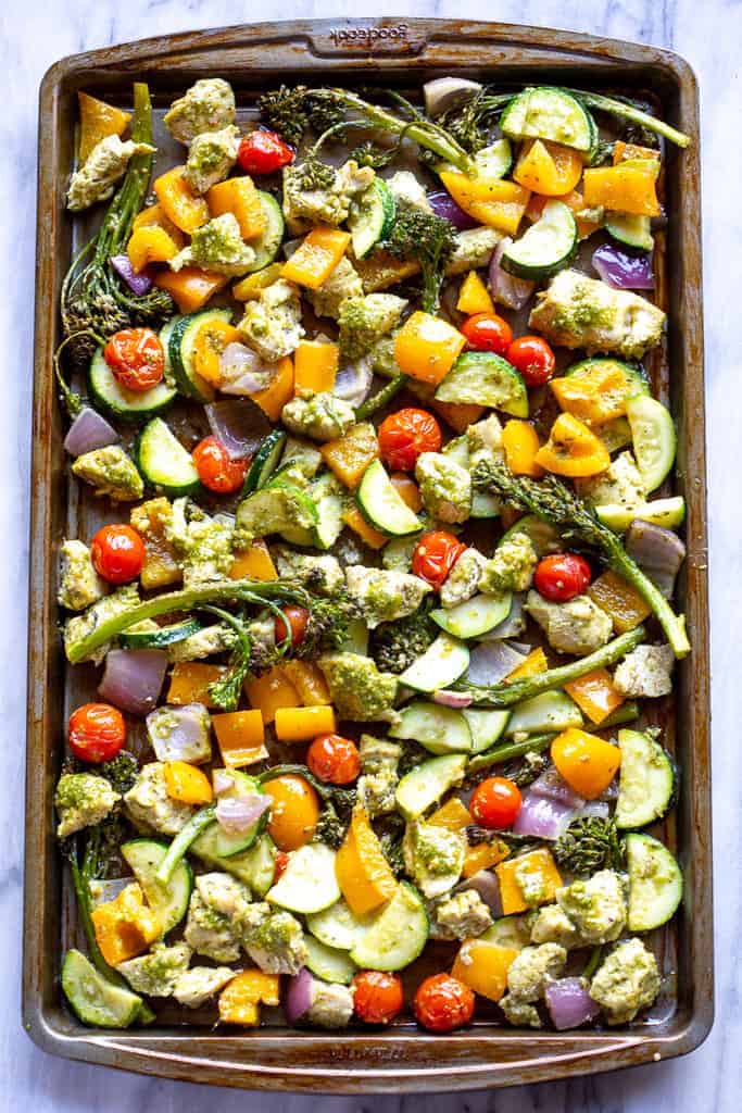 A sheet pan with pesto chicken and chopped vegetables.