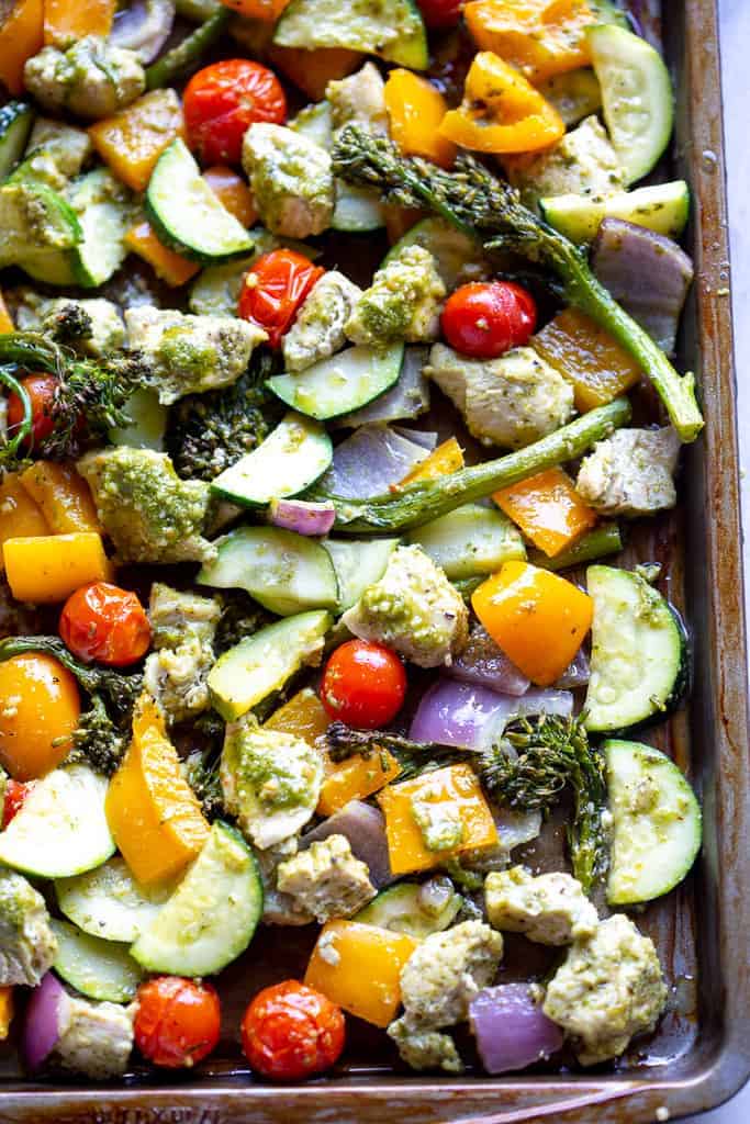Close-up for roasted chicken and vegetables in pesto sauce on a sheet pan.