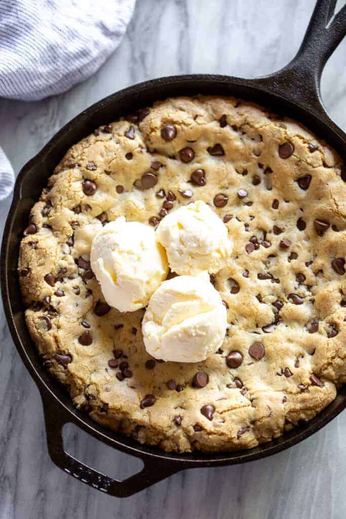 A skillet cookie baked in a cast iron skillet with three scoops of vanilla ice cream on top.