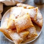 A plate full of sopapillas sprinkled with powdered sugar.
