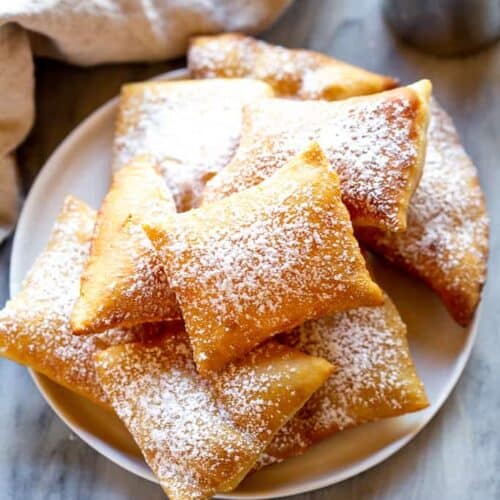 A plate full of sopapillas sprinkled with powdered sugar.