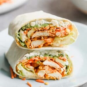Two halves of a buffalo chicken wrap stacked on each other on a white plate.