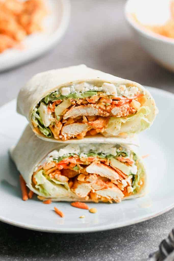 Two halves of a buffalo chicken wrap stacked on each other on a white plate.