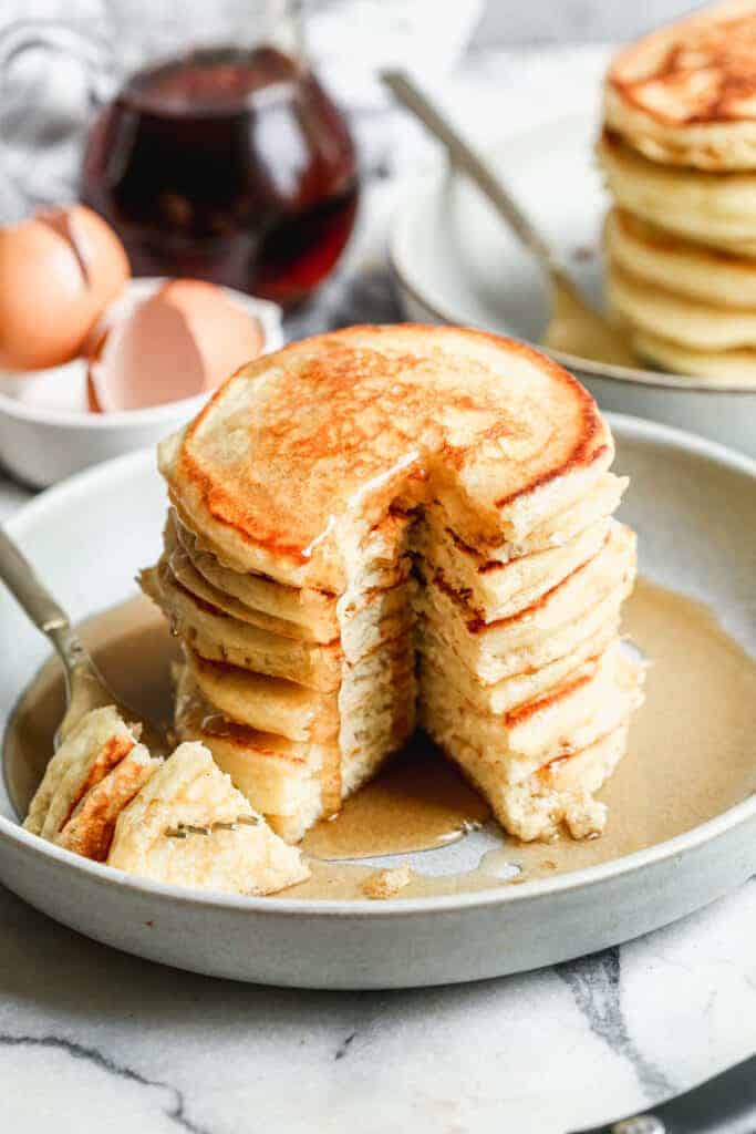 A stack of buttermilk pancakes with a big bite taken out by a fork.