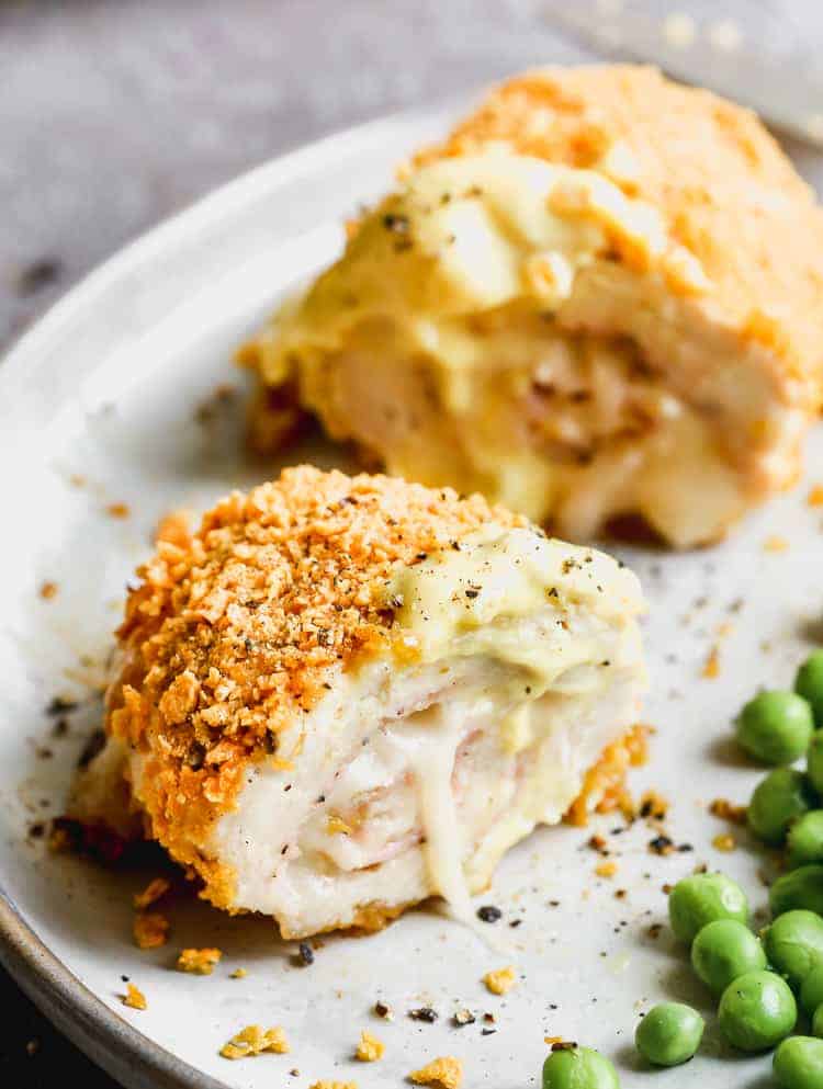Chicken cordon bleu with sauce on top, on a plate with peas.