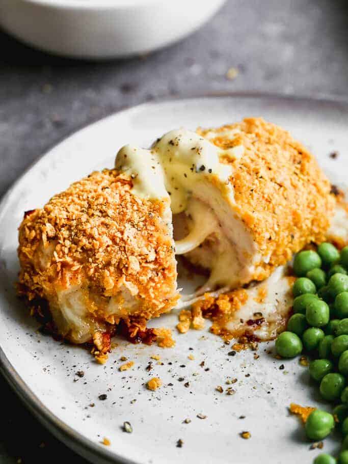 Chicken cordon bleu cut in half, on a plate with peas and sauce.