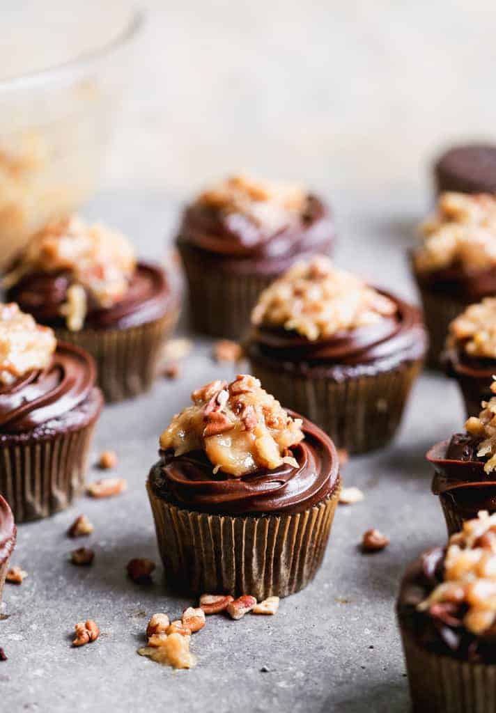 German Chocolate Cupcakes on a board with chopped pecans scattered around.