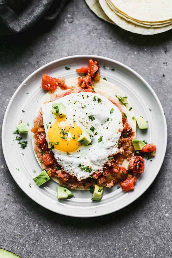 Overhead photo of huevos rancheros on a plate with chopped avocado and a fried egg.