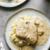 A pork chop smothered in gravy, served over mashed potatoes on a plate.