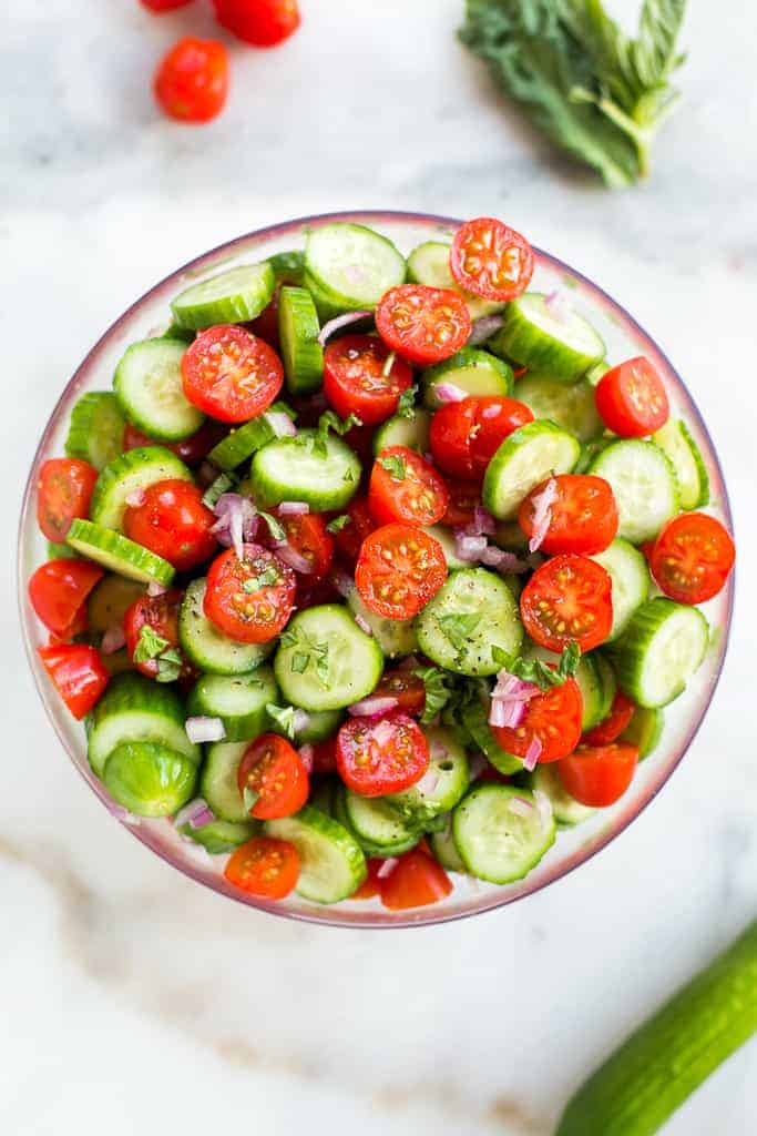 A bowl with chopped tomato, cucumber, onion and basil to make tomato cucumber salad.