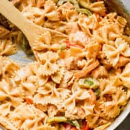 A creamy cajun chicken pasta recipe in a pan with bowtie pasta, tender bites of chicken, and peppers in a simple cajun sauce.