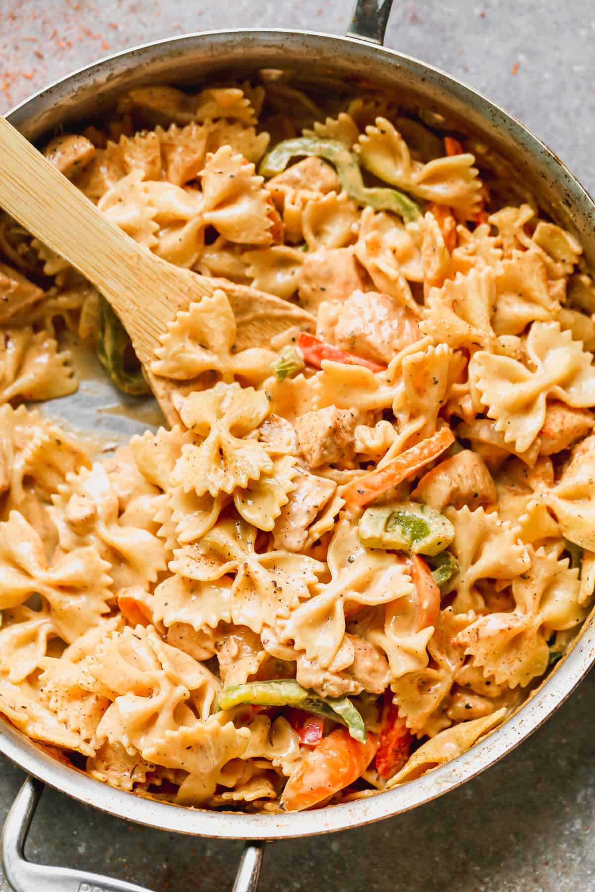 A creamy cajun chicken pasta recipe in a pan with bowtie pasta, tender bites of chicken, and peppers in a simple cajun sauce.