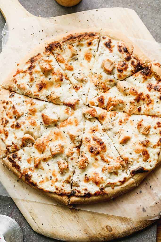 A whole chicken alfredo pizza served on a wood pizza peel.