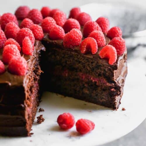 A two layer chocolate cake with raspberry filling and chocolate frosting and fresh raspberries on top.g
