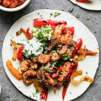 A flour torilla with fajita steak, chicken, shrimp, bell peppers, sour cream and guacamole on it.