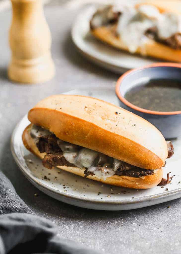 A French dip sandwich served on a plate with au jus sauce on the side.