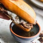 A french dip sandwich being dipped into a small bowl of au jus.