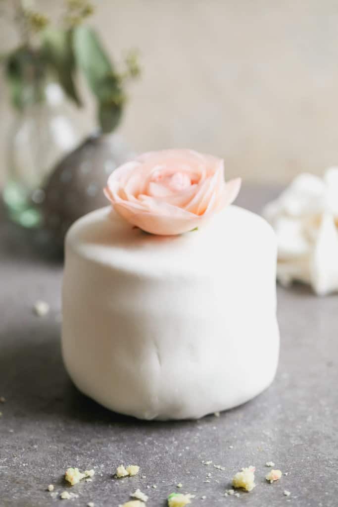 A round cake covered in homemade marshmallow fondant and topped with a pink flower.