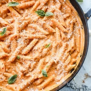 The best Penne Alla Vodka recipe in a large pan, garnished with fresh basil leaves and parmesan cheese.