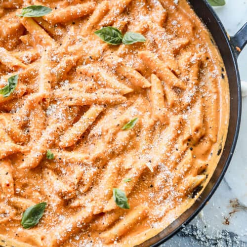 The best Penne Alla Vodka recipe in a large pan, garnished with fresh basil leaves and parmesan cheese.