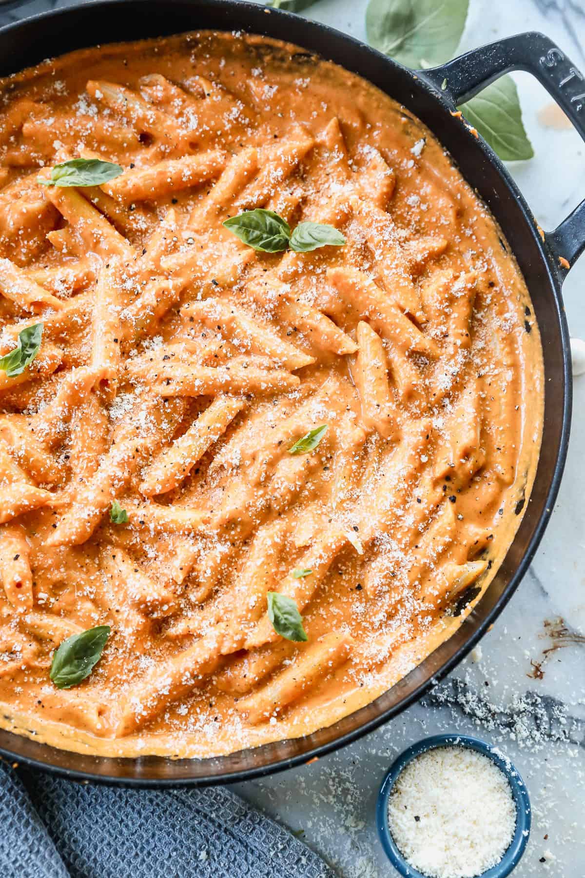 The best Penne Alla Vodka recipe in a large pan, garnished with fresh basil leaves and parmesan cheese.