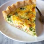 A slice of spinach and bacon quiche on a plate with a fork.