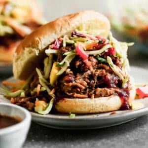 A BBQ pulled pork sandwich with slaw, in a bun, served on a plate.