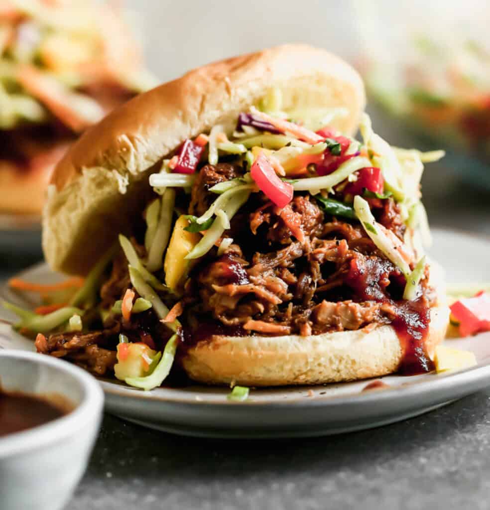 A BBQ pulled pork sandwich with slaw, in a bun, served on a plate.