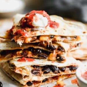 A stack of cut black bean quesadillas with salsa and sour cream on top.