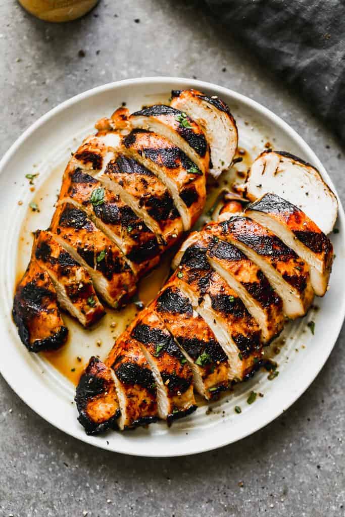 Two grilled and marinated chicken breasts, sliced, on a white plate.
