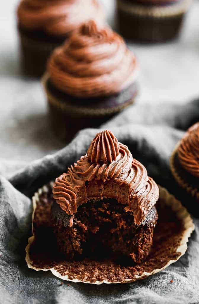 A chocolate cupcake with chocolate frosting and a big bite taken out of it. 
