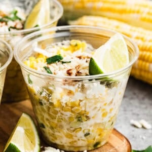A cup of homemade Esquites recipe, or Mexican Street Corn in a cup topped with cheese, cilantro, and a wedge of lime.