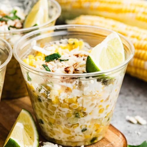 A cup of homemade Esquites recipe, or Mexican Street Corn in a cup topped with cheese, cilantro, and a wedge of lime.