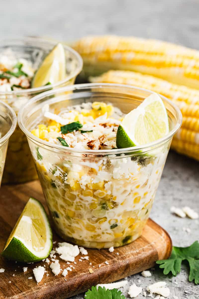 A cup of homemade Esquites recipe, or Mexican Street Corn in a cup topped with cheese, cilantro, and a wedge of lime.