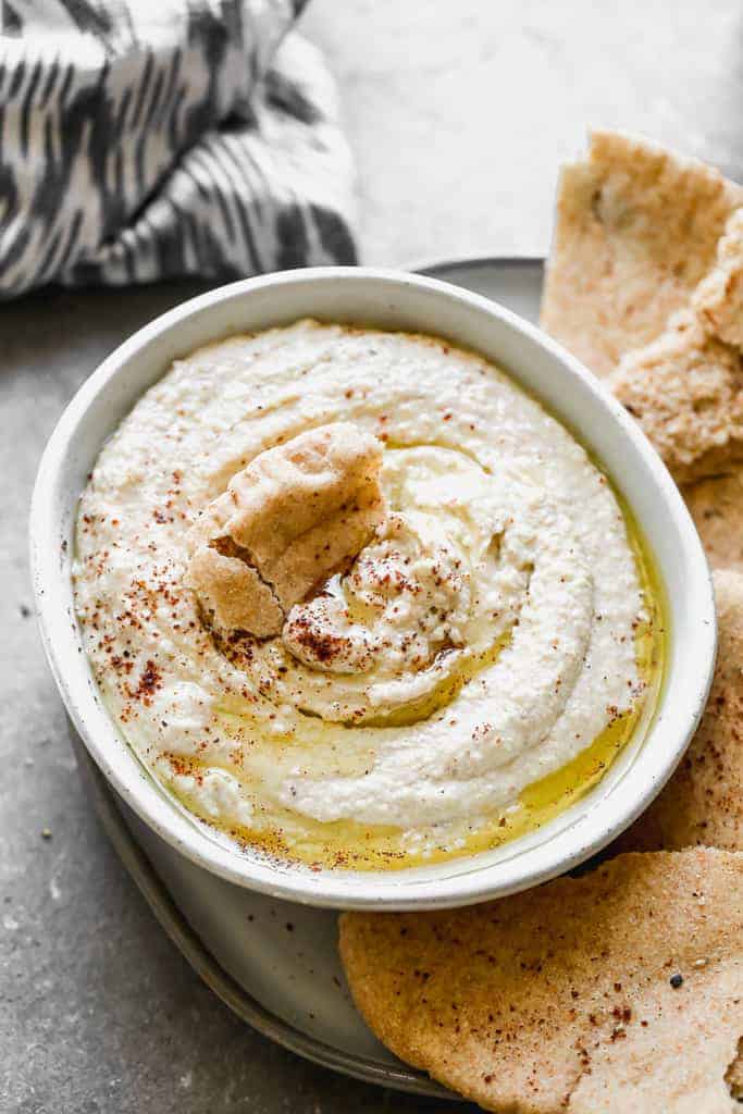 A piece if pita bread dipped into a bowl of hummus.