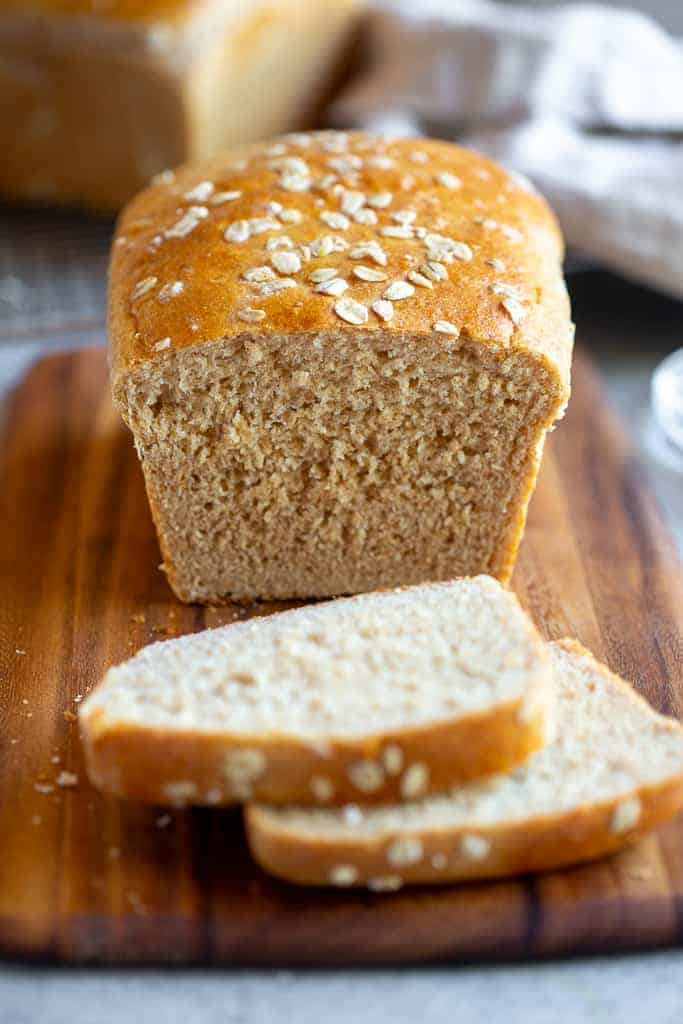 Oatmeal bread on a bread board with two slices cut from it.