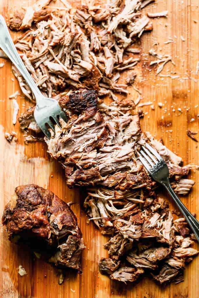 Porc cuit sur une planche à découper avec deux fourchettes déchiquetant la viande.