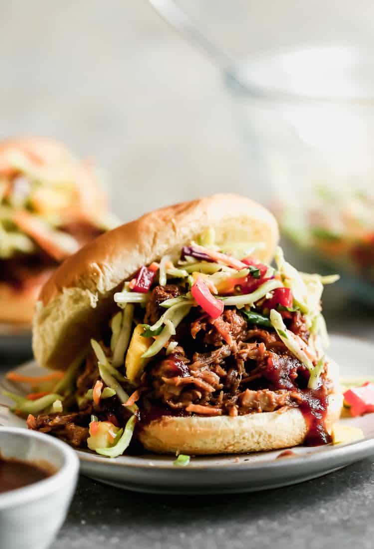 An easy BBQ Pulled Pork Sandwich served on a bun with a pineapple mango coleslaw and bbq sauce.