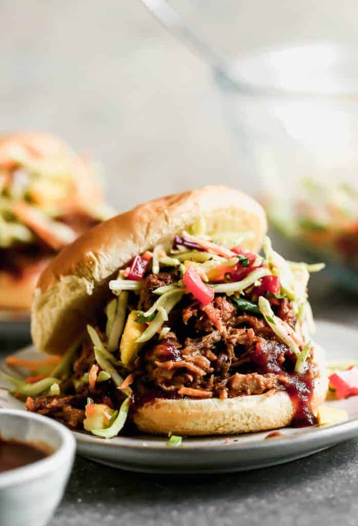 A BBQ pulled pork sandwich with slaw, in a bun, served on a plate.